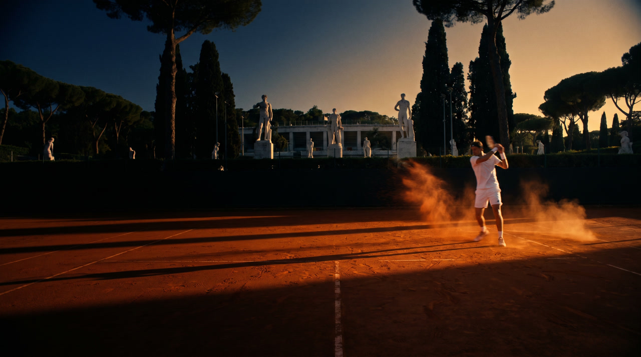 Foro Italico clay court at golden hour, Stadio dei Marmi marble statues silhouetted against a deep navy sky, cypress and umbrella pines framing the court